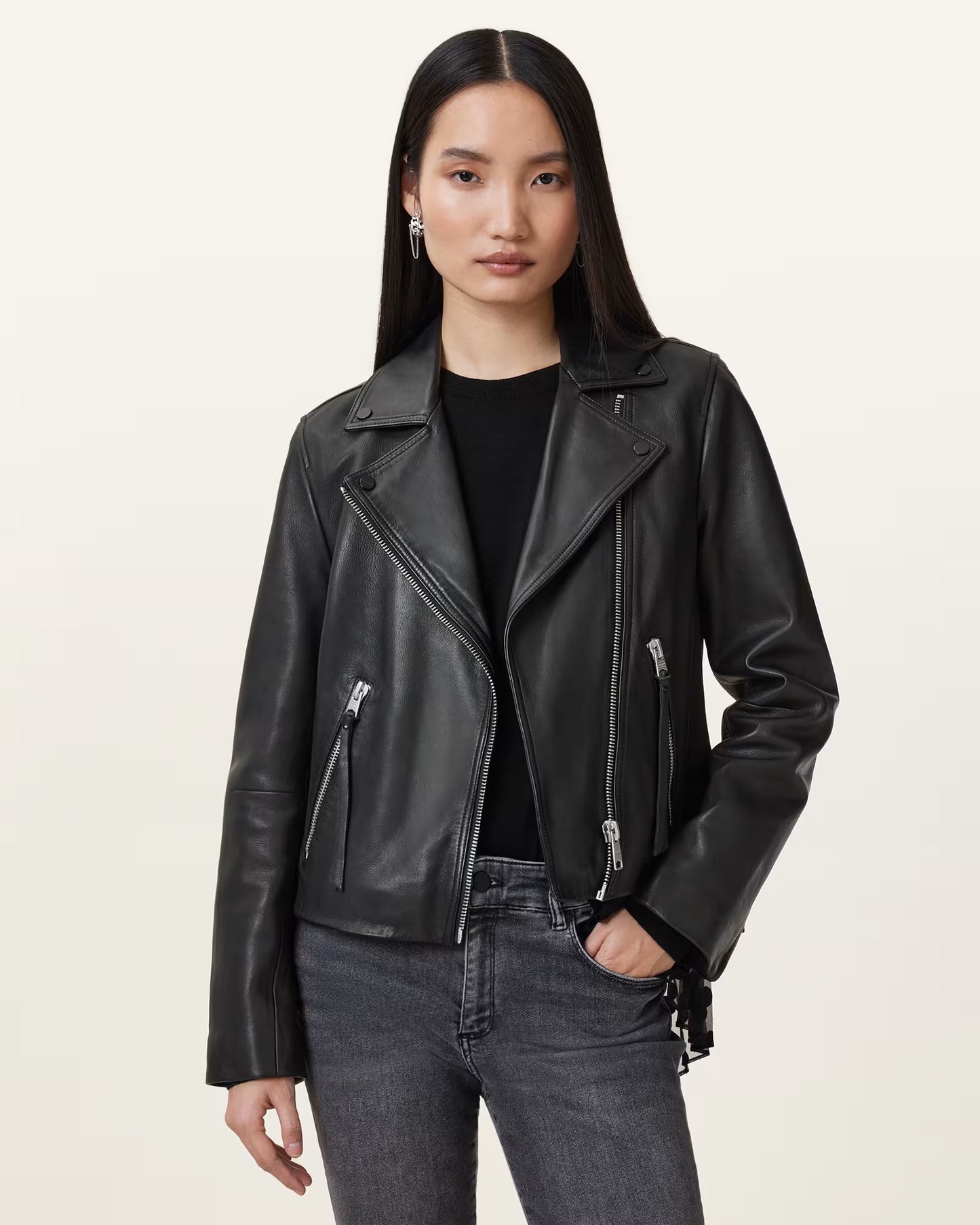 Woman wearing a black leather jacket and jeans on a plain background