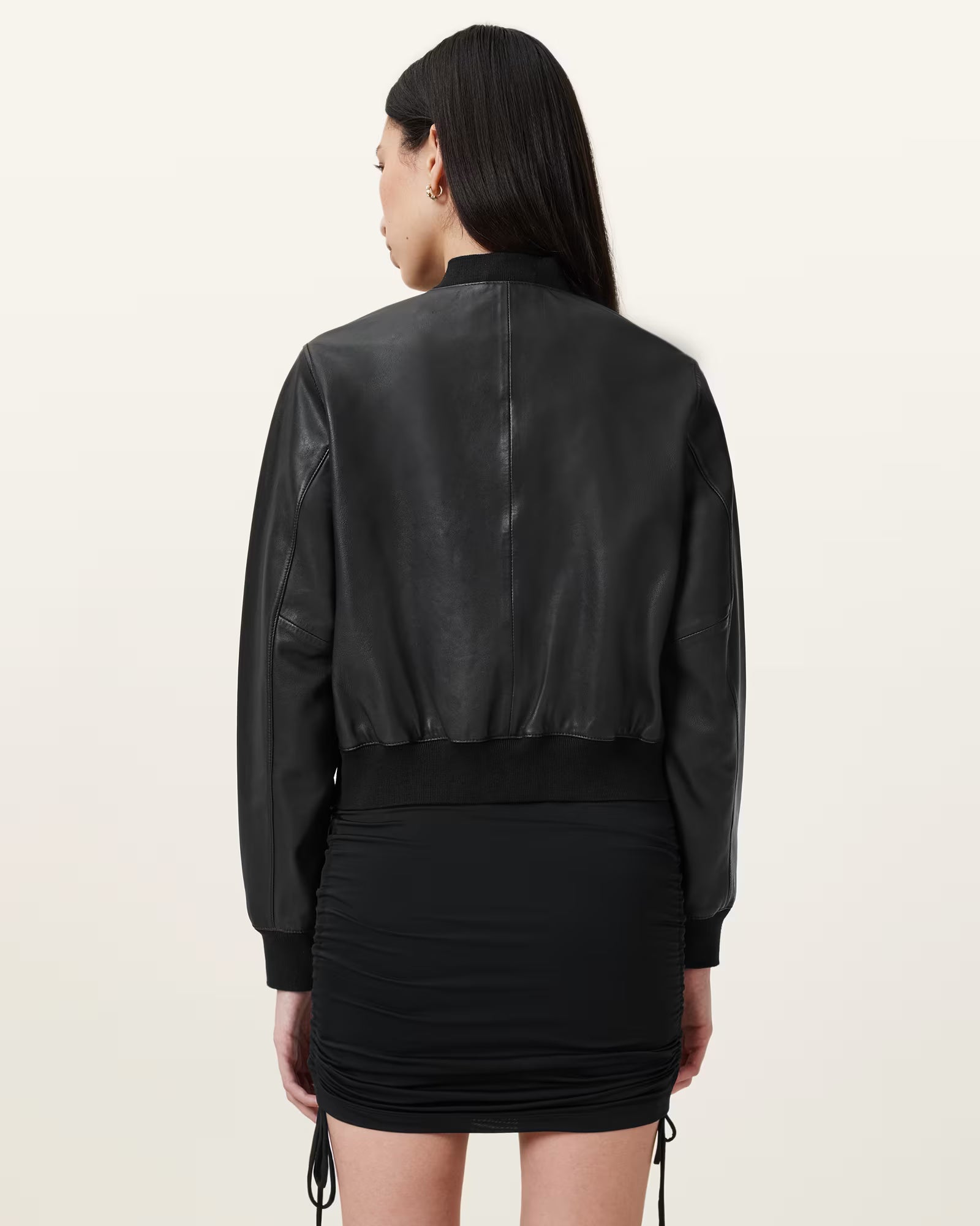 Person wearing a black leather jacket and skirt set on a beige background