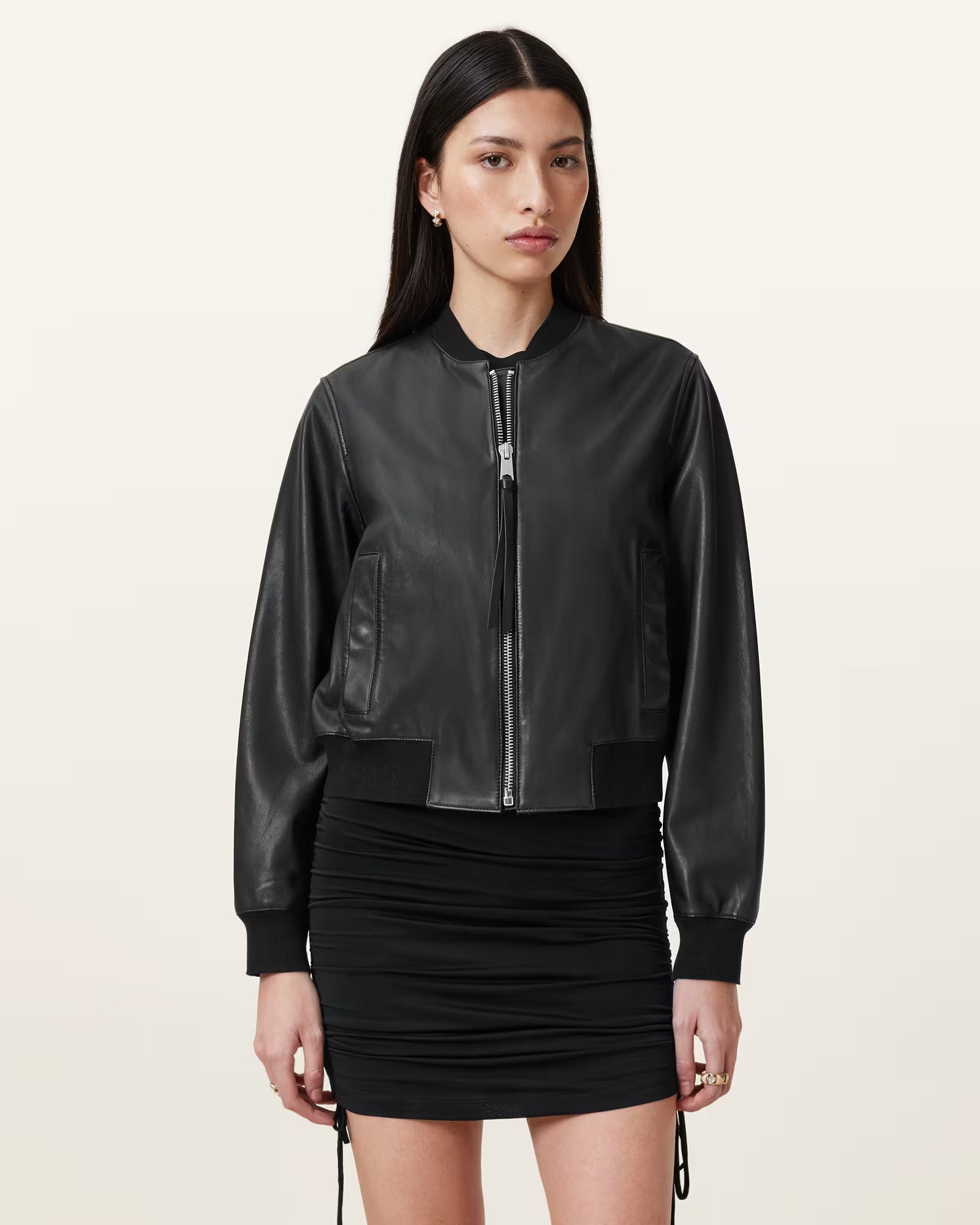 Woman wearing a black leather bomber jacket and black skirt on a beige background