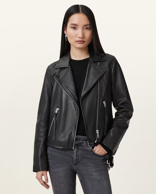 Woman wearing a black leather jacket and jeans on a plain background