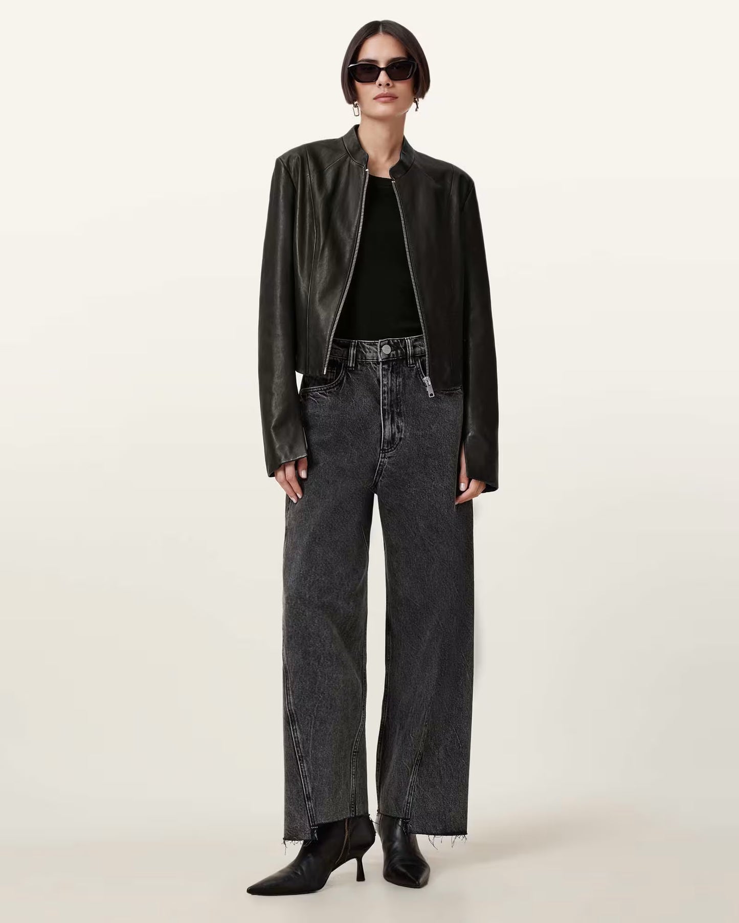 Person wearing a black leather jacket, black top, and dark jeans on a white background