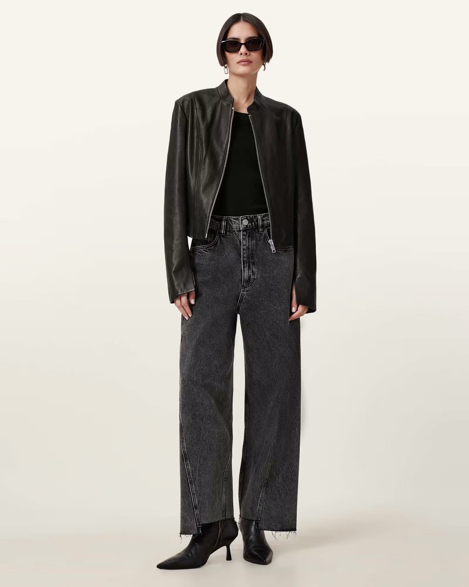 Person wearing a black leather jacket, black top, and dark jeans on a white background