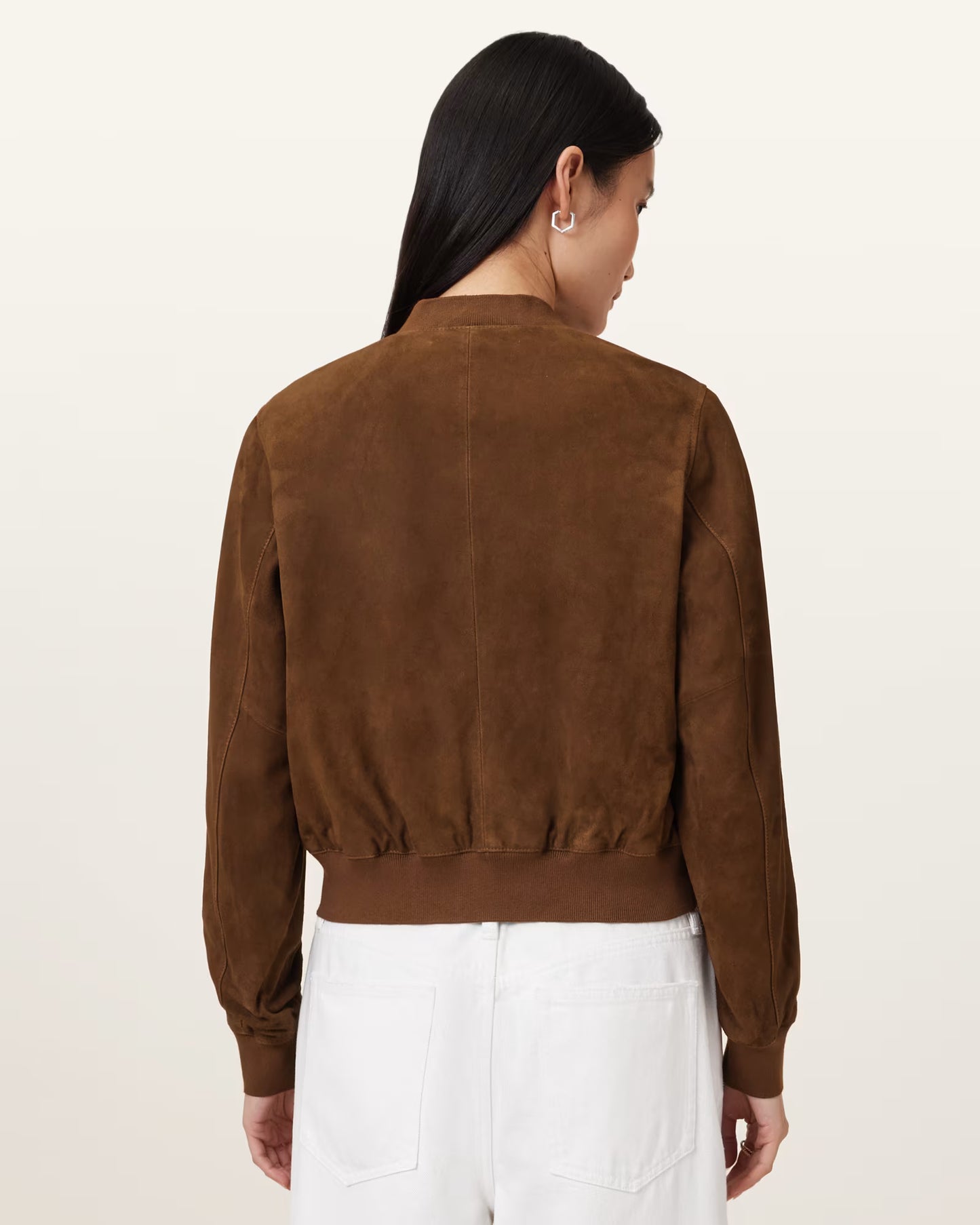 Person wearing a brown suede jacket and white pants on a beige background
