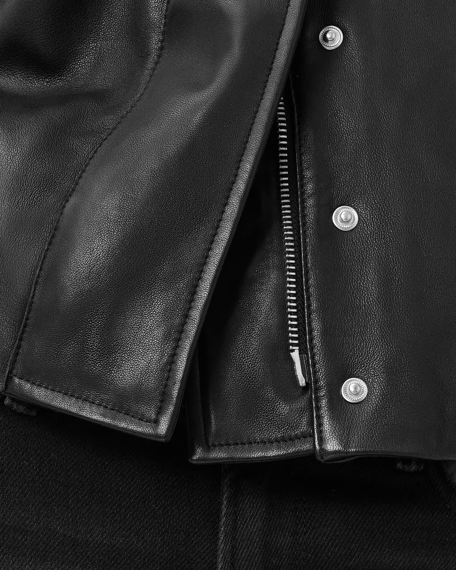 Close-up of a black leather jacket with buttons and a zipper.