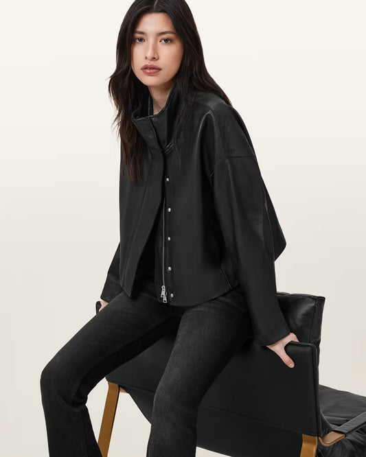 Woman wearing a black outfit sitting on a chair against a plain background