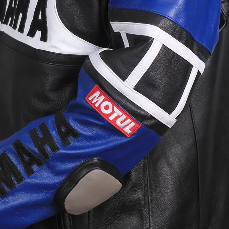 Close-up of a blue and black motorcycle glove with 'MOTUL' branding on a leather jacket background.