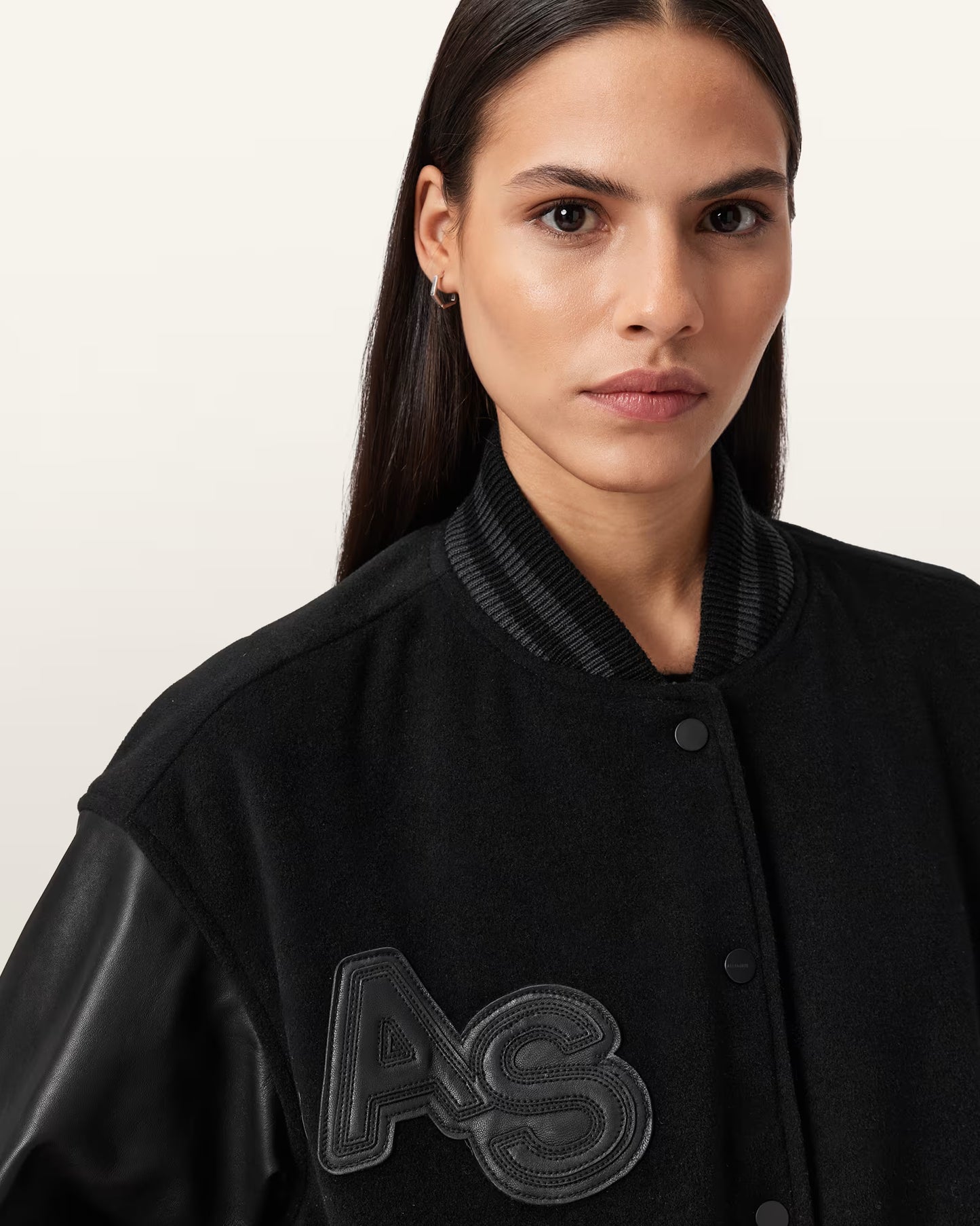Woman wearing a black varsity jacket with 'AS' logo on a plain background