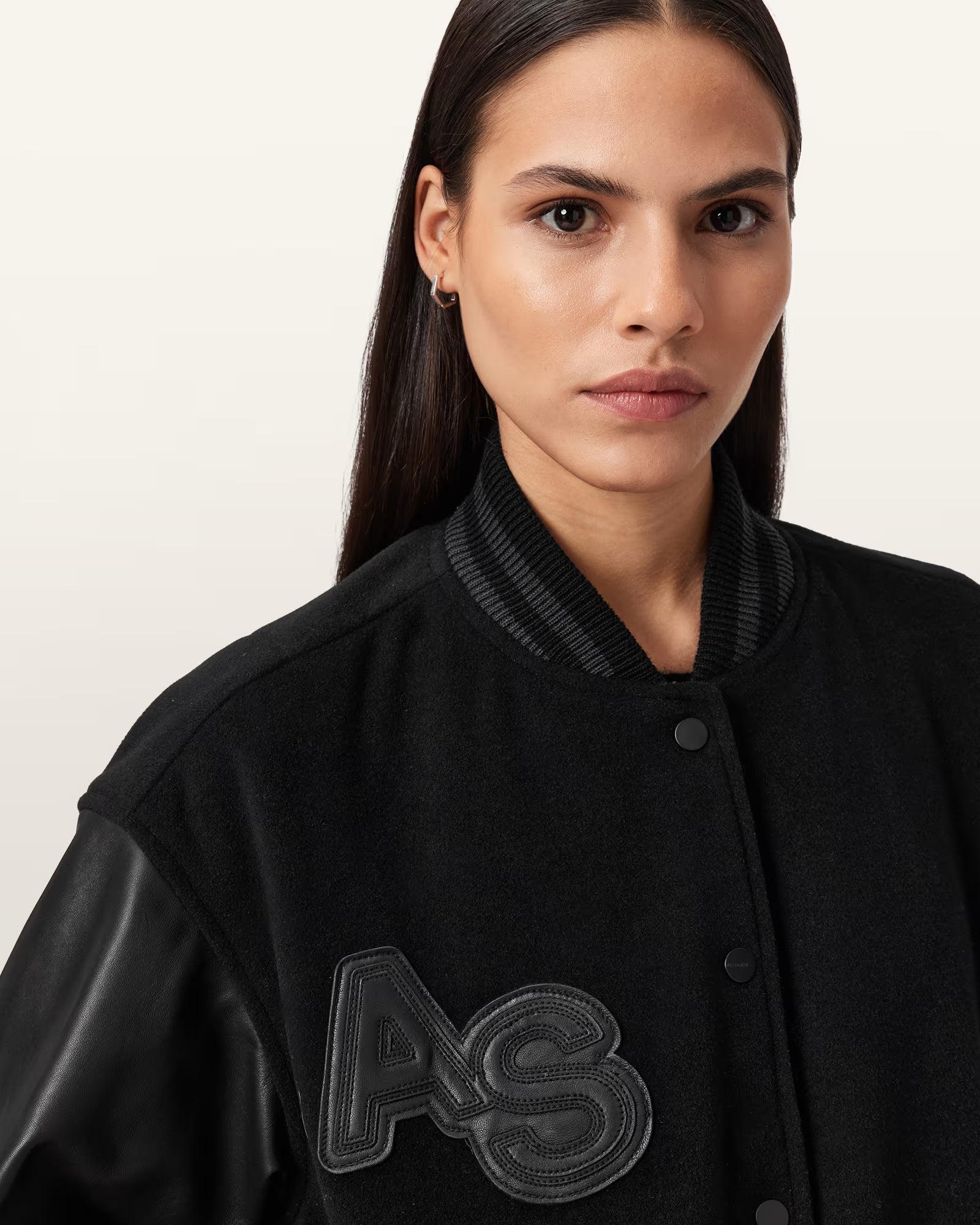 Woman wearing a black varsity jacket with 'AS' logo on a plain background