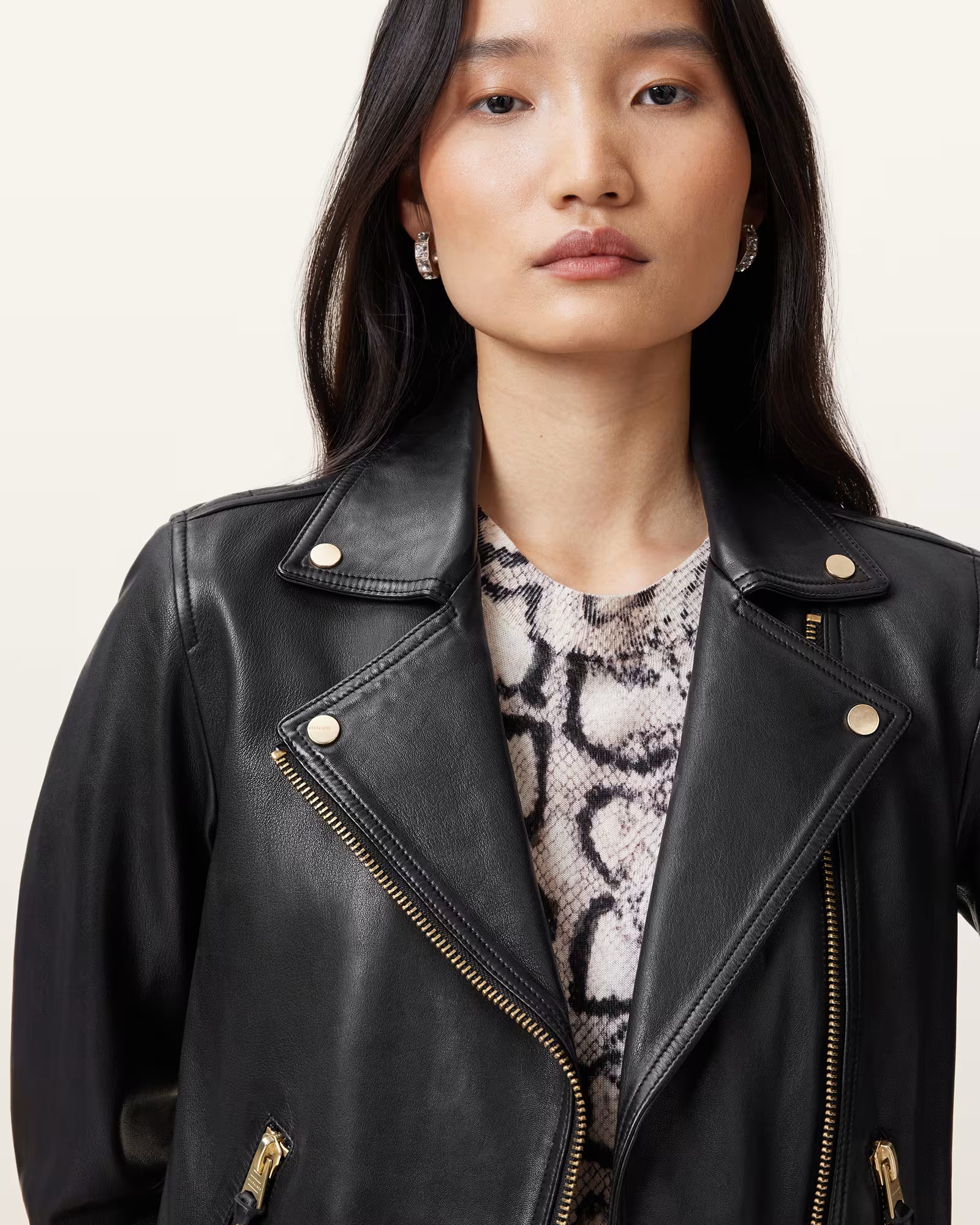 Woman wearing a black leather jacket with a snake print top underneath on a plain background