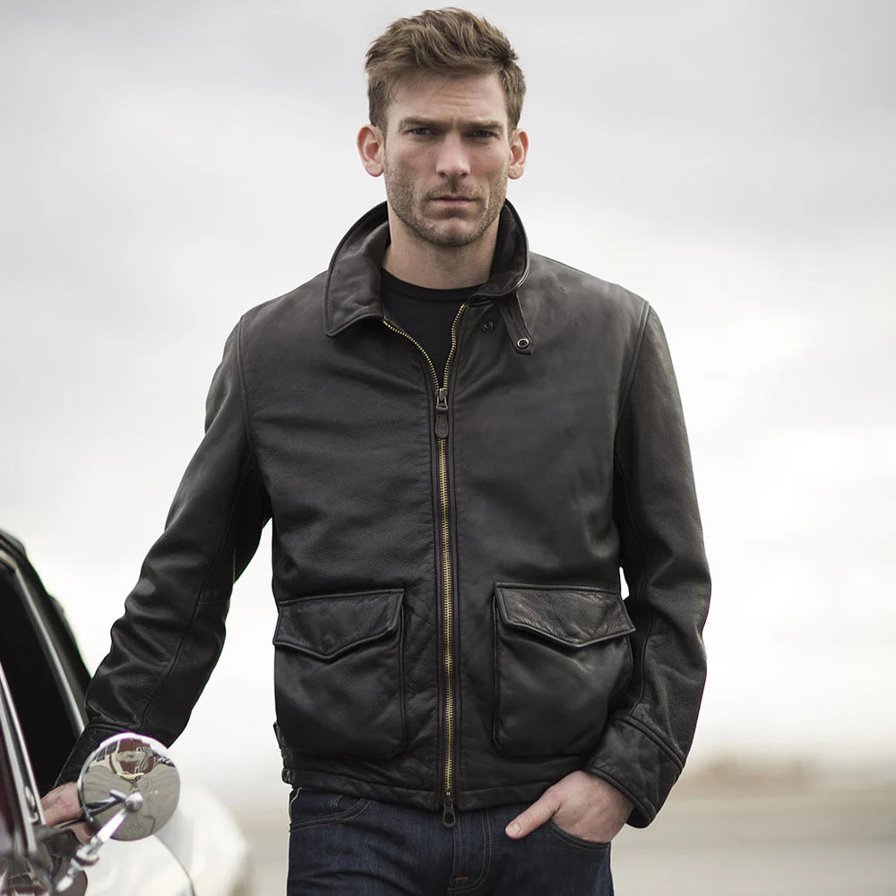 Man wearing a dark jacket standing next to a car on a plain background