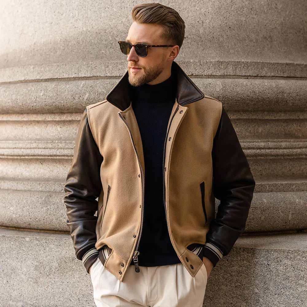Man wearing a beige and black leather jacket against a textured wall.