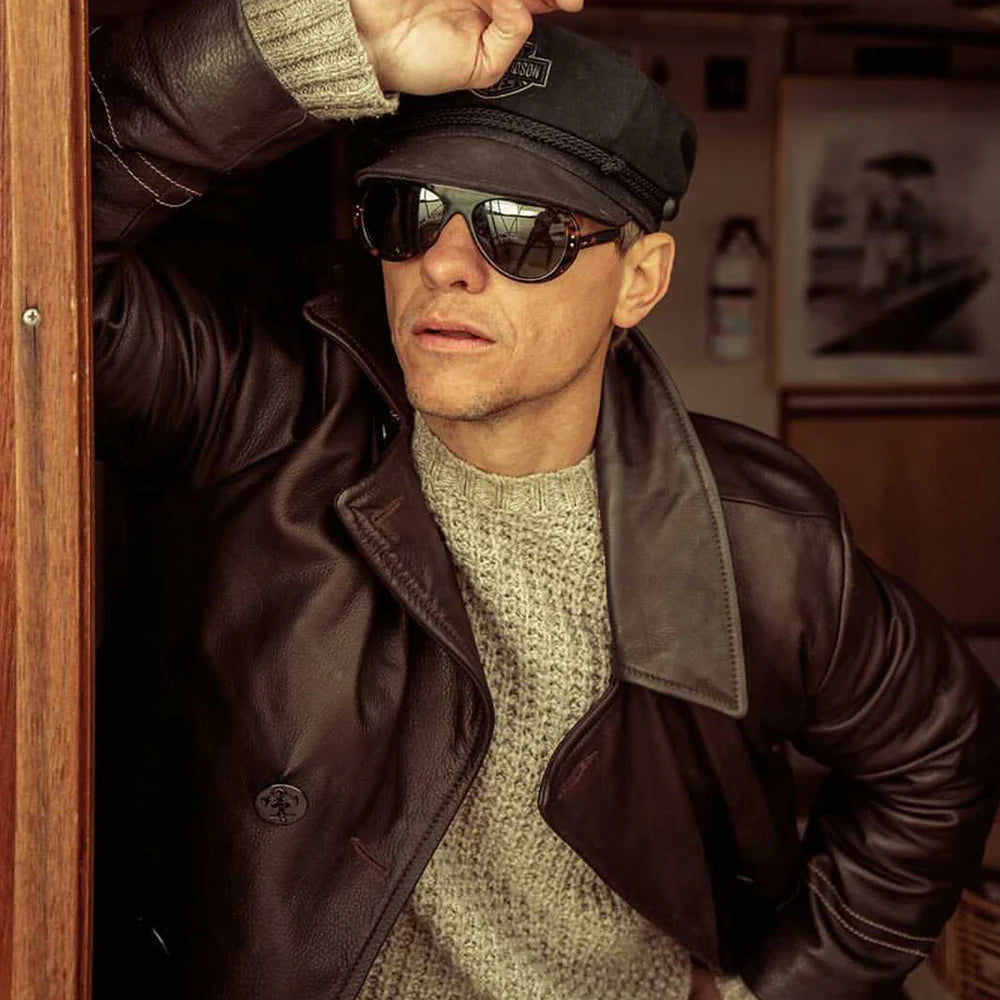 Man wearing sunglasses, a cap, and a leather jacket in an indoor setting.