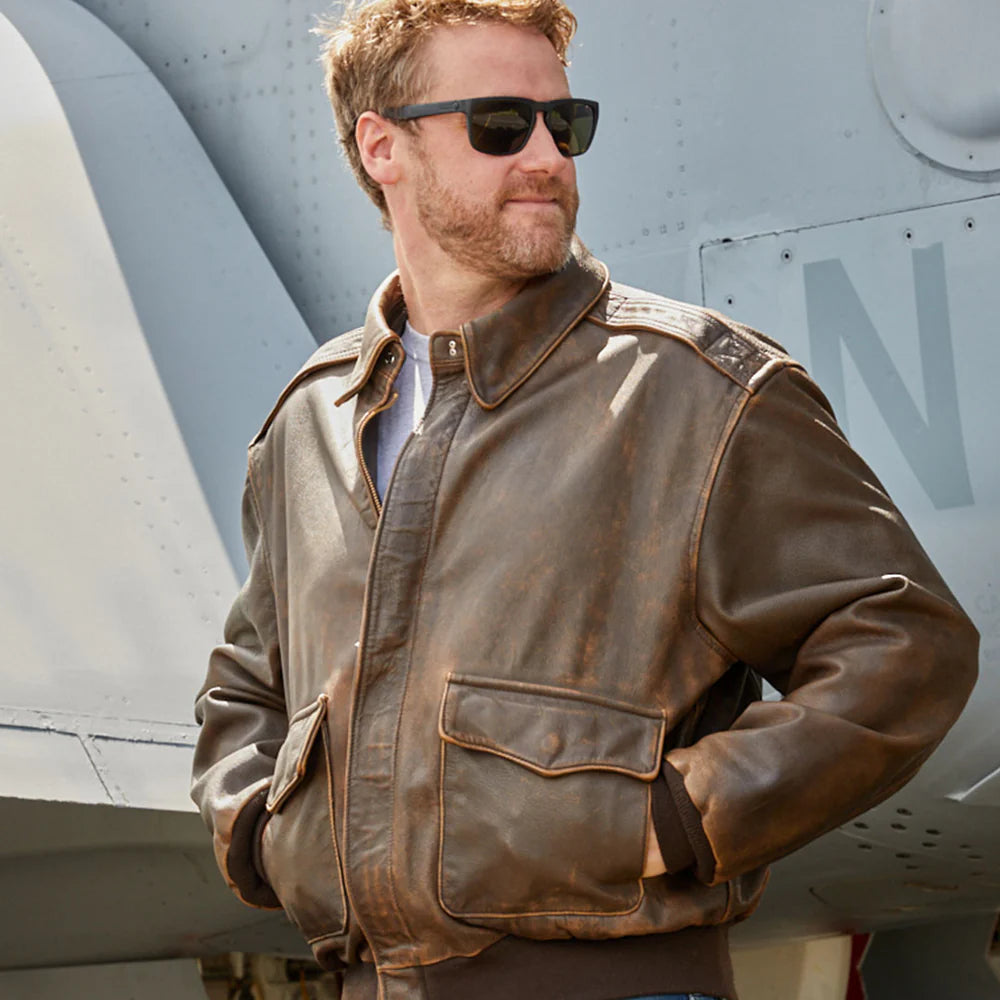 Man wearing a brown leather jacket and sunglasses standing in front of an airplane.