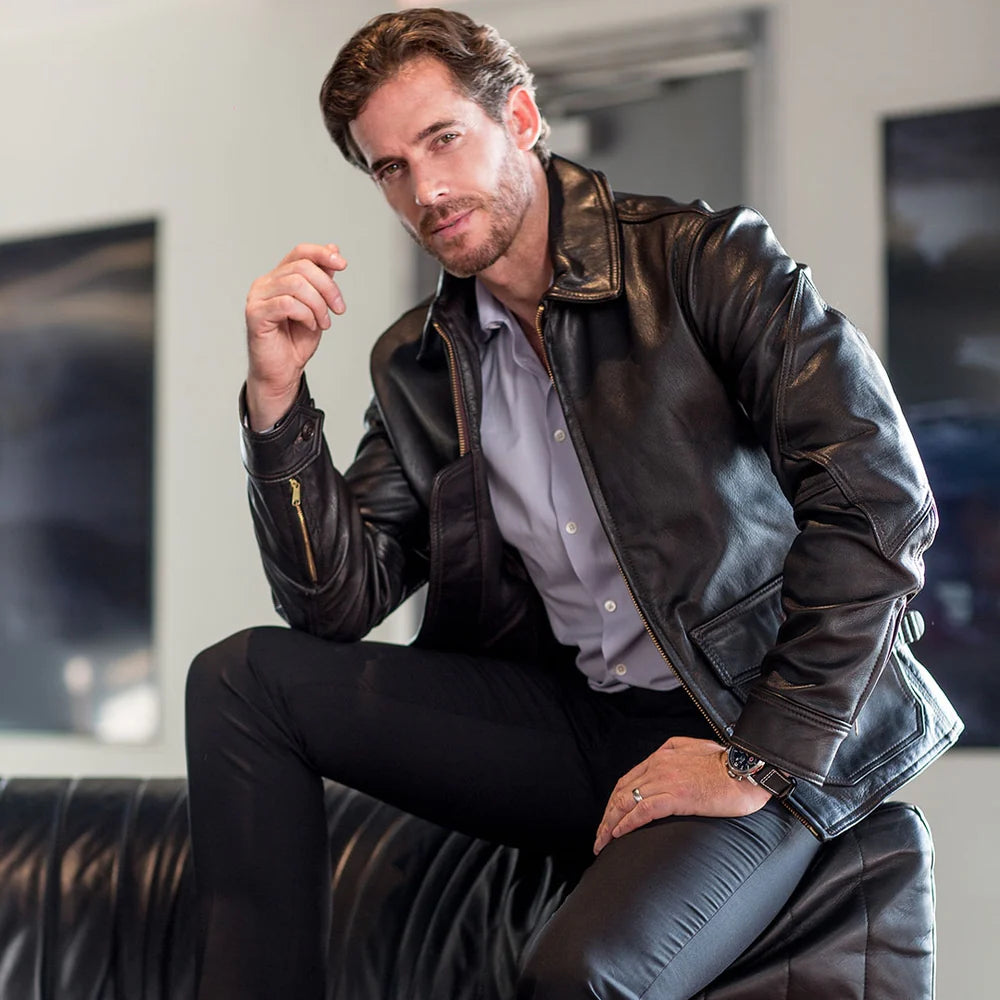Man wearing a black leather jacket sitting on a black leather chair.