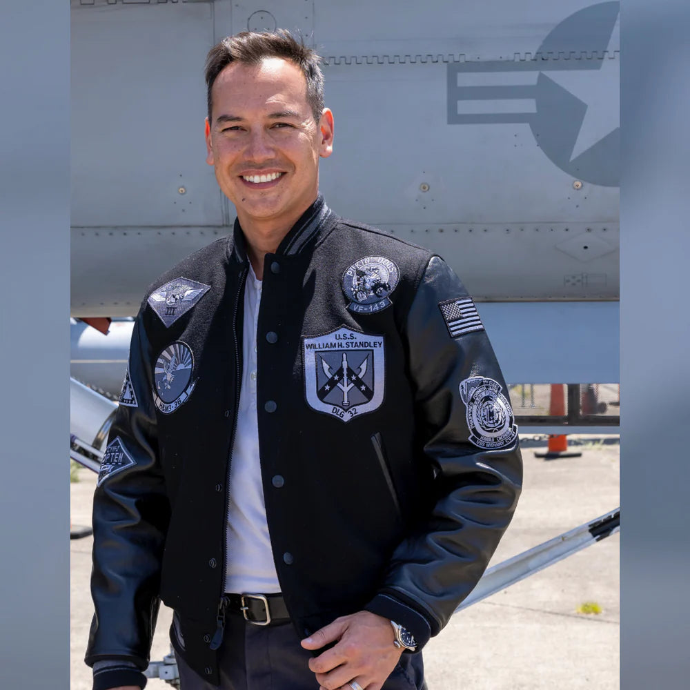 Man wearing a black jacket with patches in front of an airplane