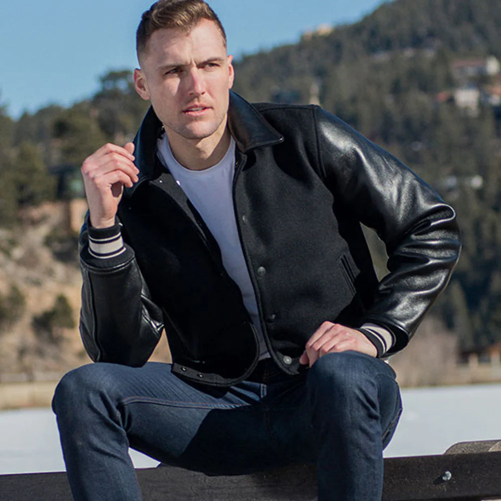 Man wearing a black leather jacket sitting outdoors with mountains in the background